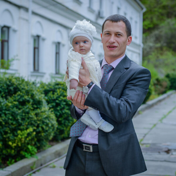 Dziecko po chrzcie w objęciach ojca — fotograf Warszawa studiyasveta